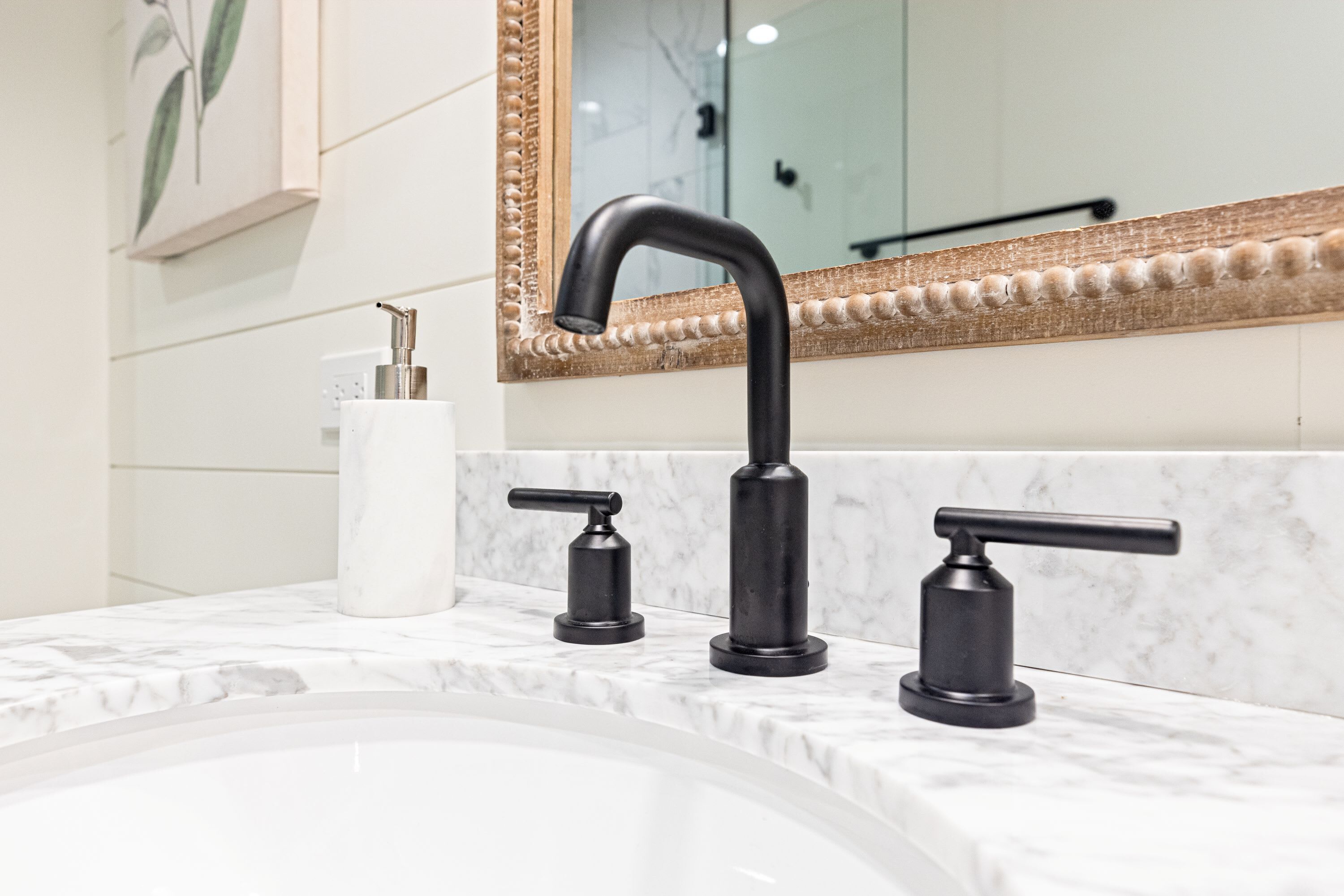 Une salle de bain avec un lavabo en marbre, un robinet noir et un miroir doté d’un cadre décoratif.