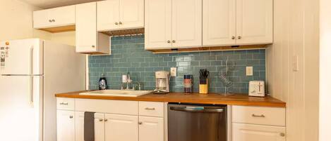 Cocina con armarios blancos, salpicadero de azulejos azules, lavavajillas de acero inoxidable y encimera de madera.