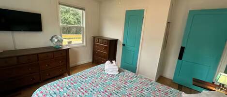 Un dormitorio con una cama, un tocador, un ventilador de techo y una ventana.