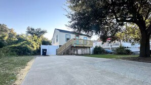 A residential property with a concrete driveway, a wooden deck, and a house with a white exterior and blue trim. - SandyPaws-0.5mi ToSound & 1mi ToBeach PetFriendly! (Kill Devil Hills)