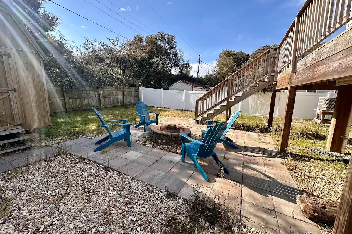 Un patio aménagé dans le jardin, avec un foyer, des sièges d’extérieur et une terrasse en bois.