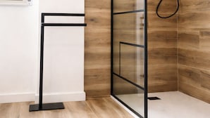 Un box de ducha moderno con puerta de cristal, pared de madera y suelo blanco.