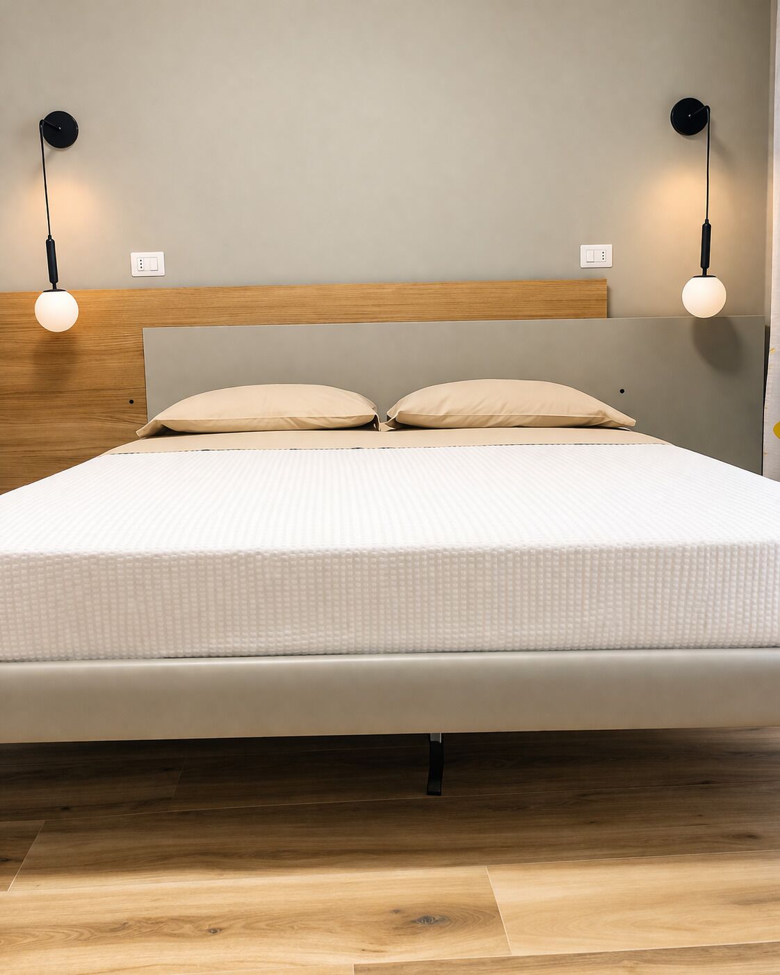 A modern bed with a wooden headboard, two bedside lamps, and a light switch on the wall.
