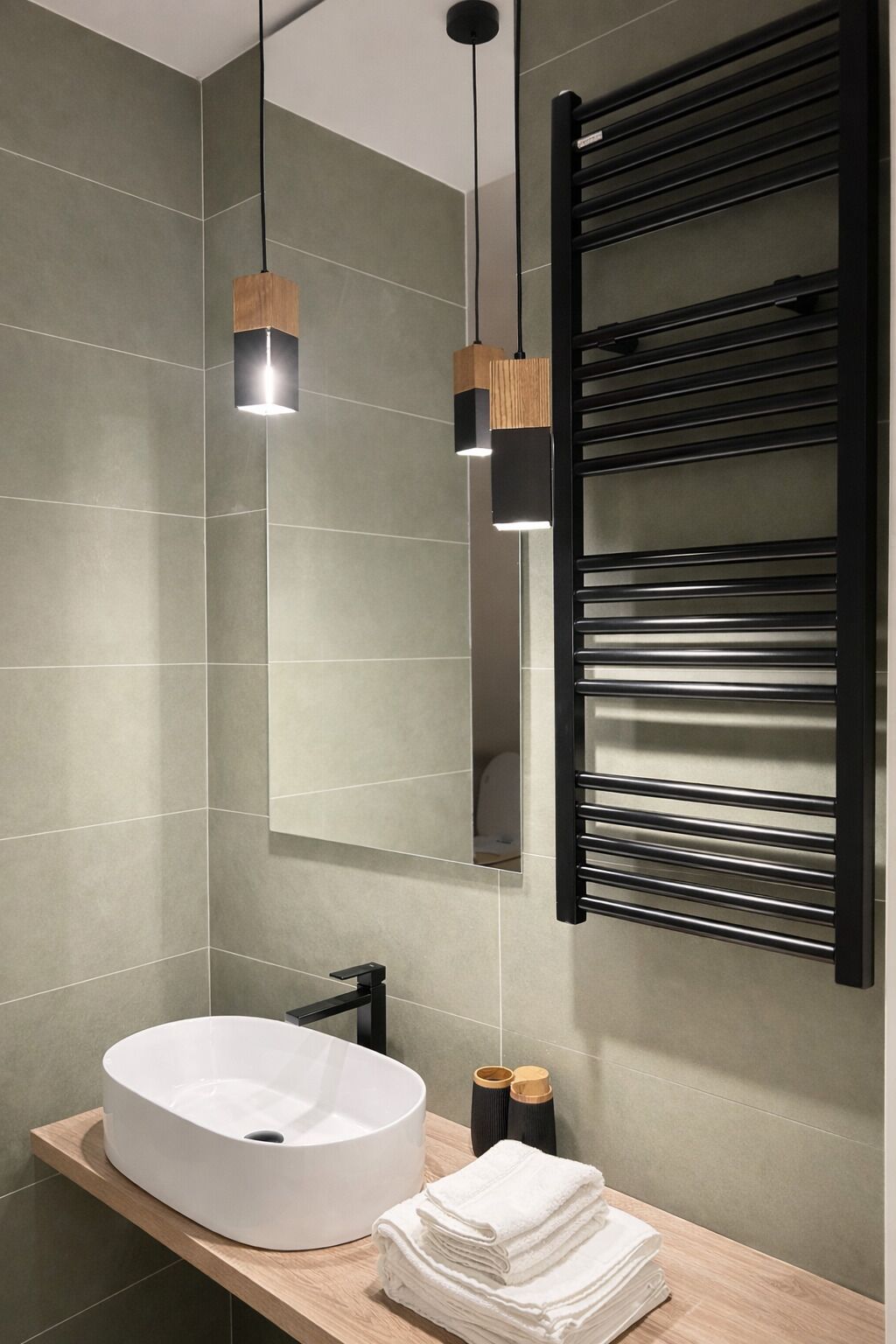 Un baño moderno con un lavamanos grande de color blanco, dos lámparas colgantes, una pila de toallas y un perchero negro.