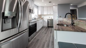 A modern kitchen with stainless steel appliances, white cabinetry, and a grey wooden floor.