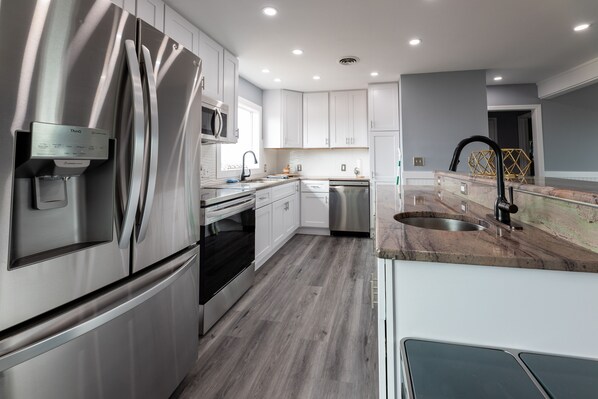 A modern kitchen with stainless steel appliances, white cabinetry, and a granite countertop.