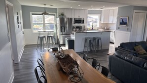 A modern kitchen with white cabinets, a central island with stools, a dining table with chairs, and a black leather sofa.