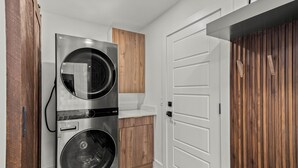 A laundry room with stacked washers and dryers, a wooden cabinet, and a white door.
