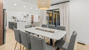 A modern dining area with a white table, grey upholstered chairs, and a woven pendant light.