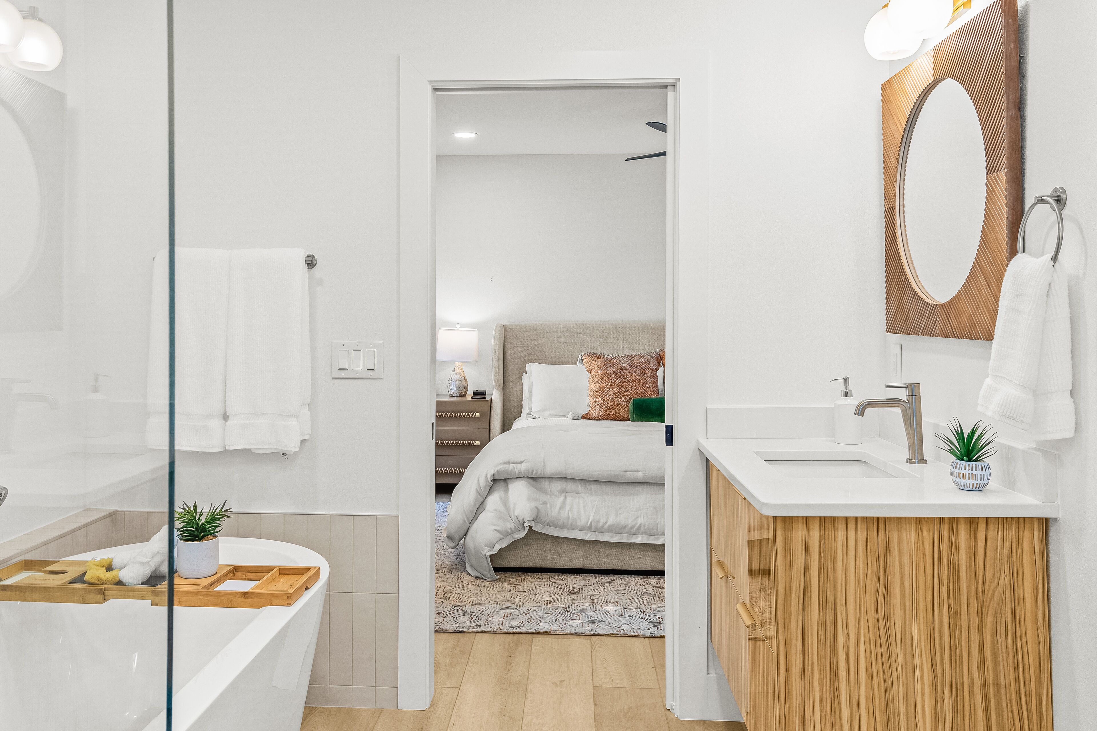 Un baño moderno con separador de vidrio, tocador de madera, lavamanos blanco y espejo.