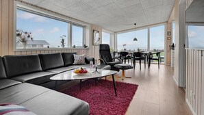 A spacious living area with a black leather sofa, a white coffee table, and a red shag rug. There is a dining area with a table and chairs, and large windows offering a view of the outside. - Amazing home in Sjølund with WiFi (Sjølund)