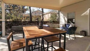 Eine Terrasse im Freien mit einem Holztisch und -stühlen, einem überdachten Sitzbereich und Blick auf den Garten.