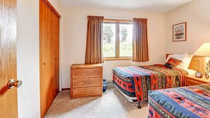 Ein Schlafzimmer mit zwei Betten, einer Holzkommode, einem Fenster mit Vorhängen und einem gerahmten Bild an der Wand.