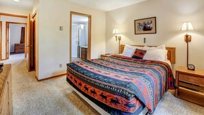Ein Schlafzimmer mit einem großen Bett, zwei Nachttischlampen, einem Nachttisch, einer hölzernen Kommode und einer Tür zu einem anderen Raum.