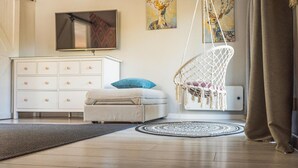Een moderne woonkamer met een witte bank, een hangstoel, een televisie en kunstwerken aan de muur.