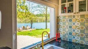Een keuken met een groot raam dat uitkijkt op een meer, een wastafel met een gouden kraan en een betegelde achterwand met een geometrisch patroon.