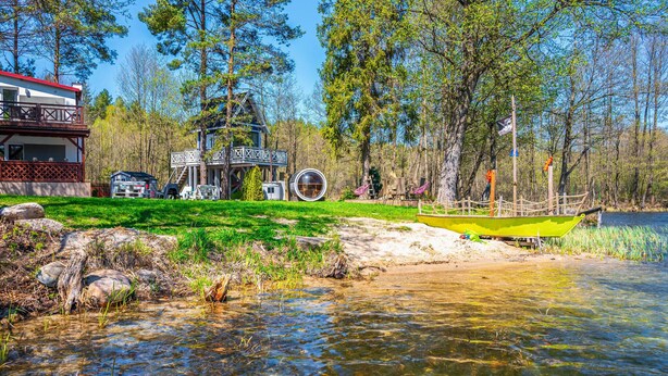 Een vakantiehuis aan de rivier met een terras, een ronde glazen constructie en een klein aanlegsteiger met een gele boot.