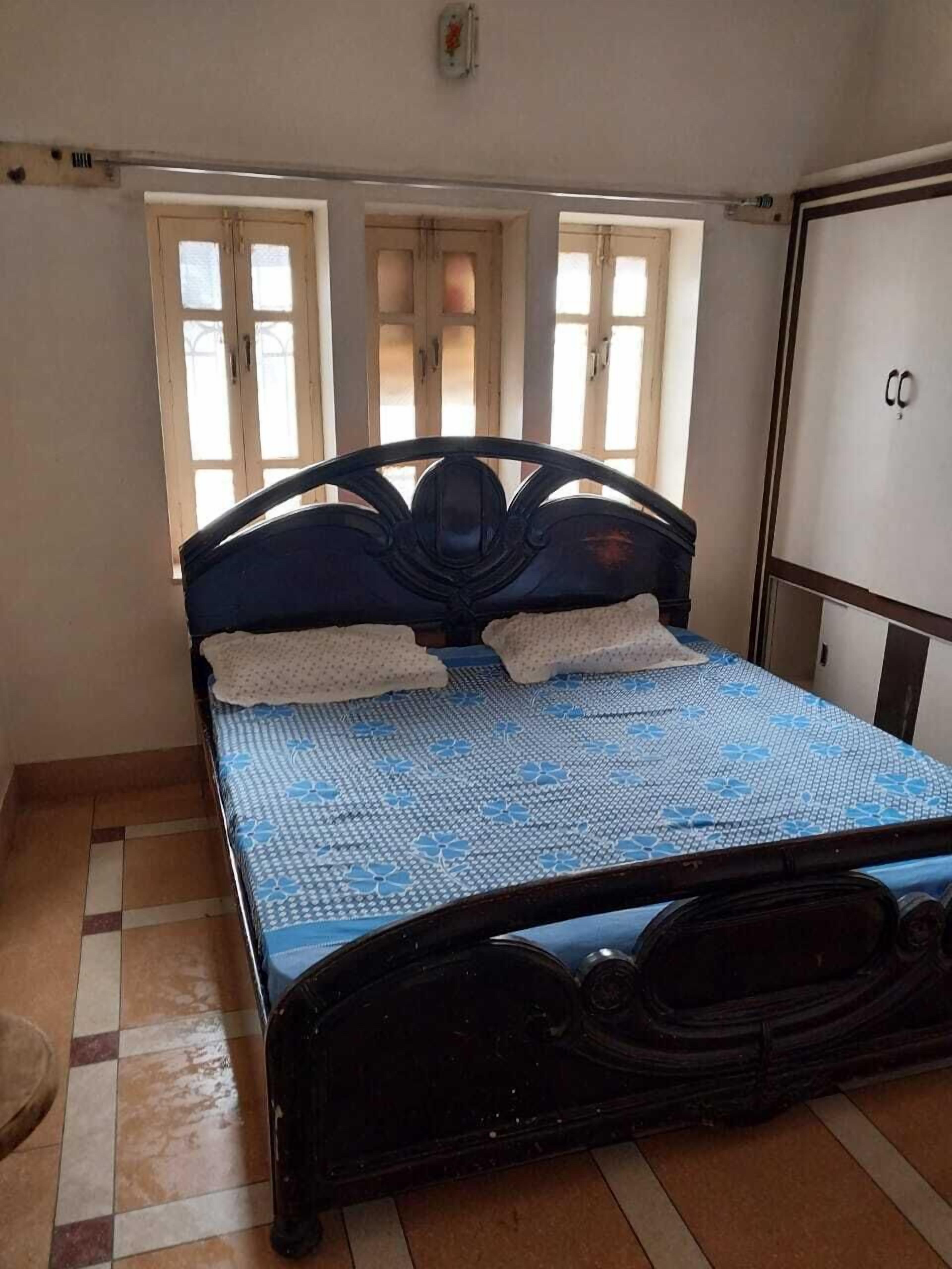 Una camera da letto con un letto, due finestre, un armadio e un pavimento piastrellato.