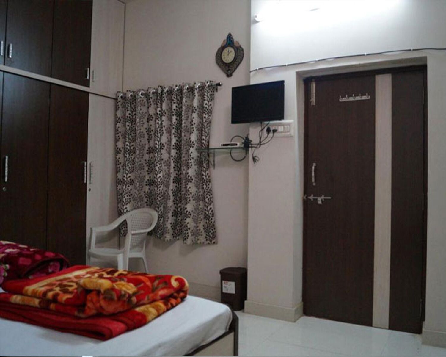 A bedroom with a bed, a chair, a wardrobe, a television, and a door.