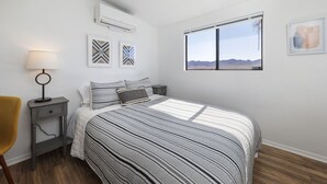 Une chambre à coucher avec un lit, une table de chevet, une lampe et une fenêtre donnant sur les montagnes.