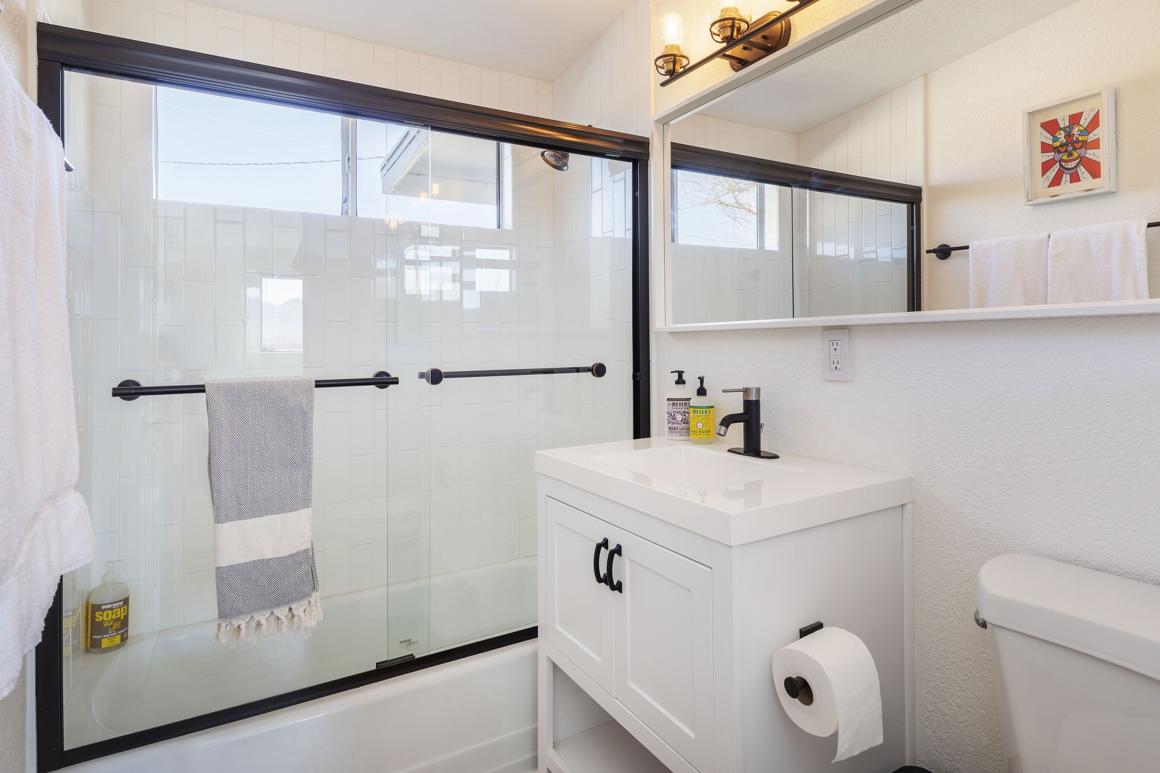 A bathroom with a glass-enclosed shower, a white sink with a mirror above it, and a toilet.