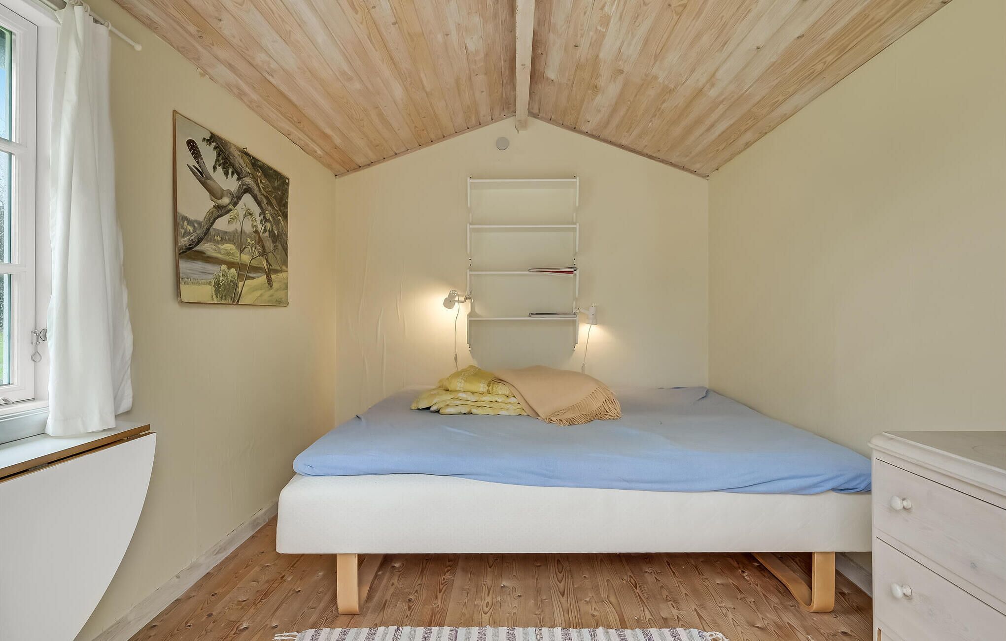 Un dormitorio con cama, un tocador blanco, un cuadro en la pared y techo de madera.