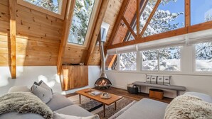Un intérieur de chalet chaleureux avec une cheminée, des murs en bois et de grandes fenêtres.