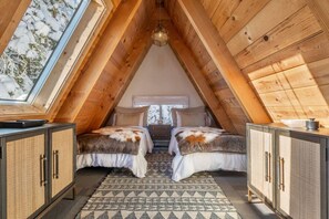 Quarto de sótão acolhedor, com vigas de madeira, duas camas com mantas de pele sintética, um tapete estampado e um claraboia.