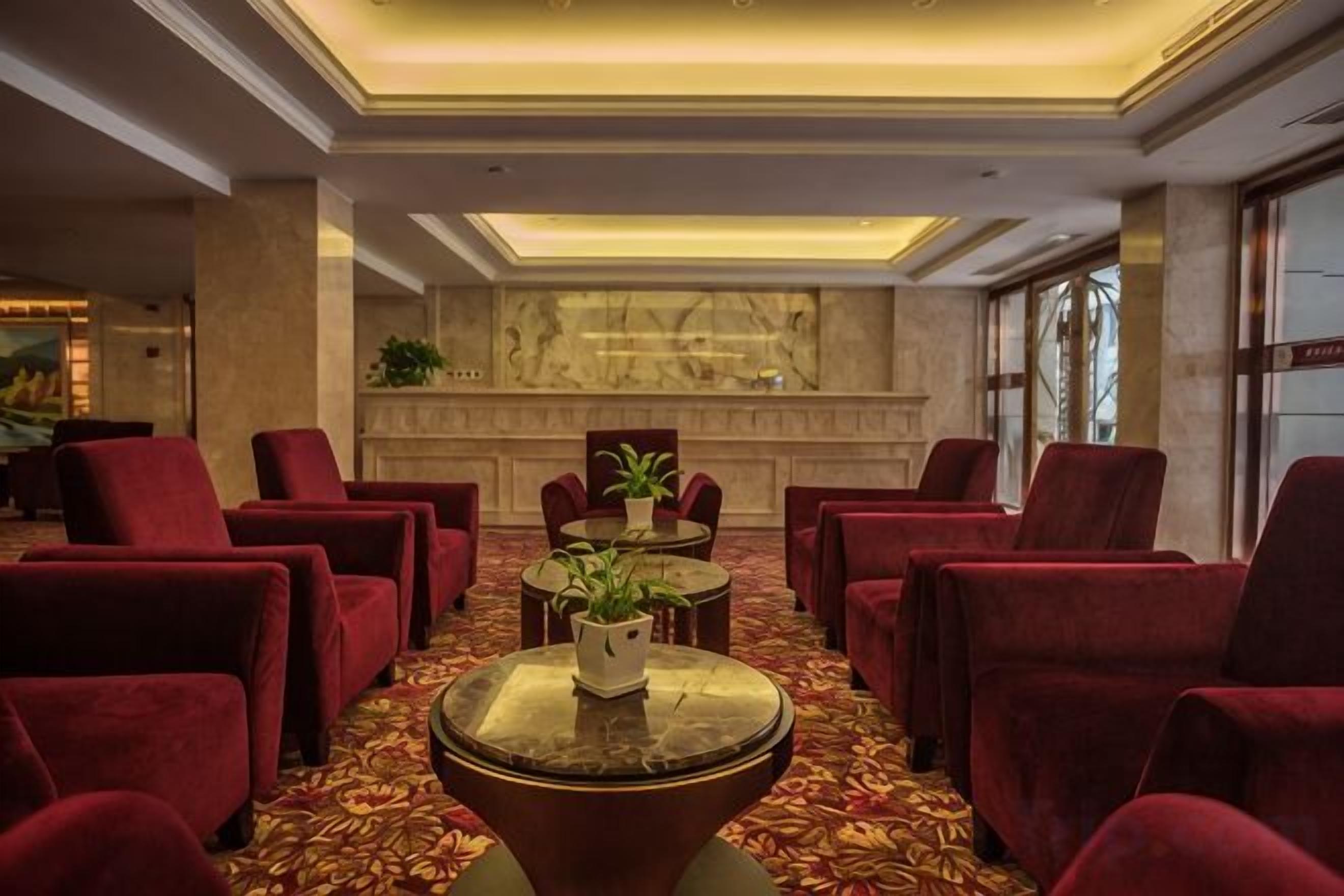 Un hall con sillones tapizados de rojo, una mesa redonda central con una planta y una pared de mármol al fondo.