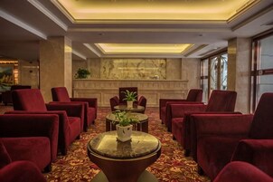 Un hall con sillones tapizados de rojo, una mesa redonda central con una planta y una pared de mármol al fondo.