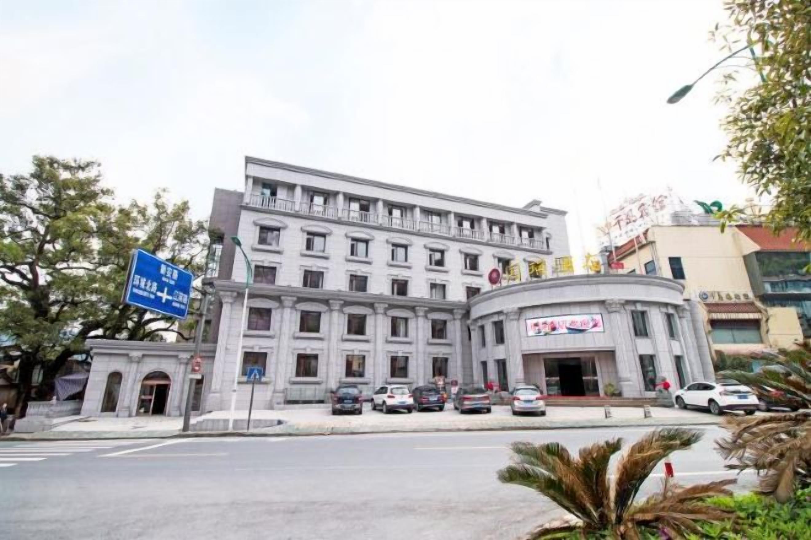 A multi-story building with a central entrance, surrounded by parked cars and a clear sky.