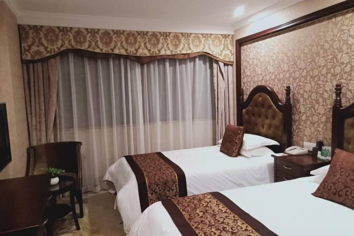A hotel room with two beds, a wooden headboard, a desk, and a chair.