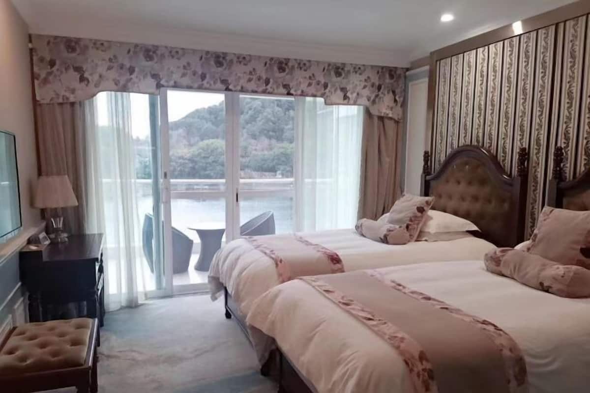 A hotel room with two beds, a TV, a desk, and a view of a body of water.