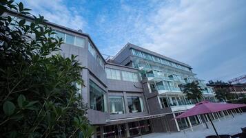 A modern hotel with a glass facade, outdoor seating area, and a covered walkway.