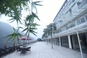Una terraza al aire libre con mesas y sillas, un edificio de cristal y montañas al fondo.