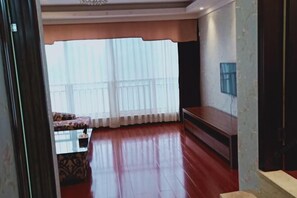 A spacious living room with a large window, a sofa, a coffee table, and a TV mounted on the wall. - Guorui Hotel (Jiande)