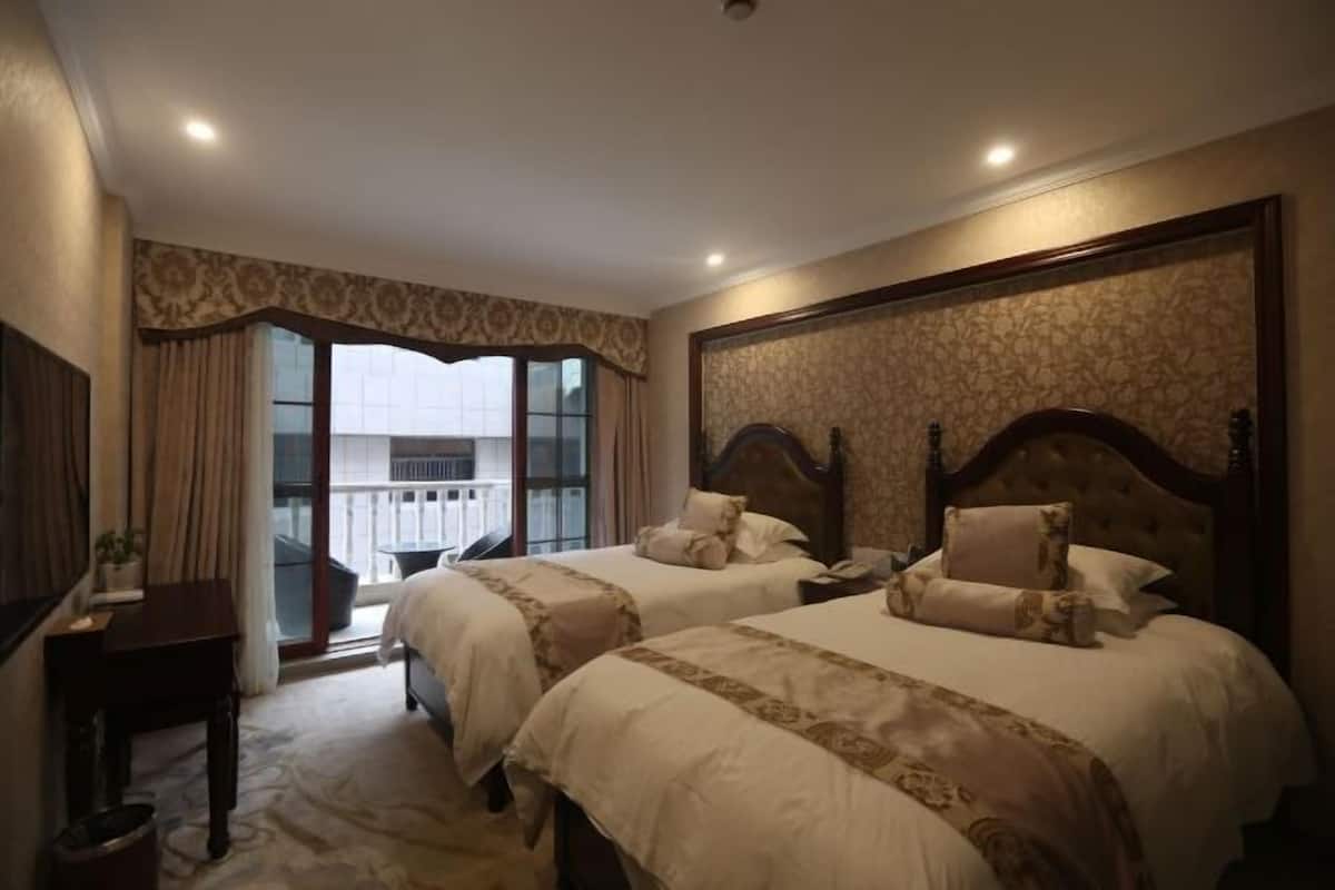 A hotel room with two beds, a desk, and a balcony with a view.