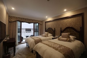Habitación de hotel con dos camas, un escritorio y un balcón con vistas.