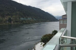 A river with a building on the right, a balcony with glass railings, and a mountainous backdrop. - Guorui Hotel (Jiande)