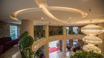 Un vestíbulo de hotel de varios niveles con una gran lámpara de araña, alfombra roja y una escalera moderna.