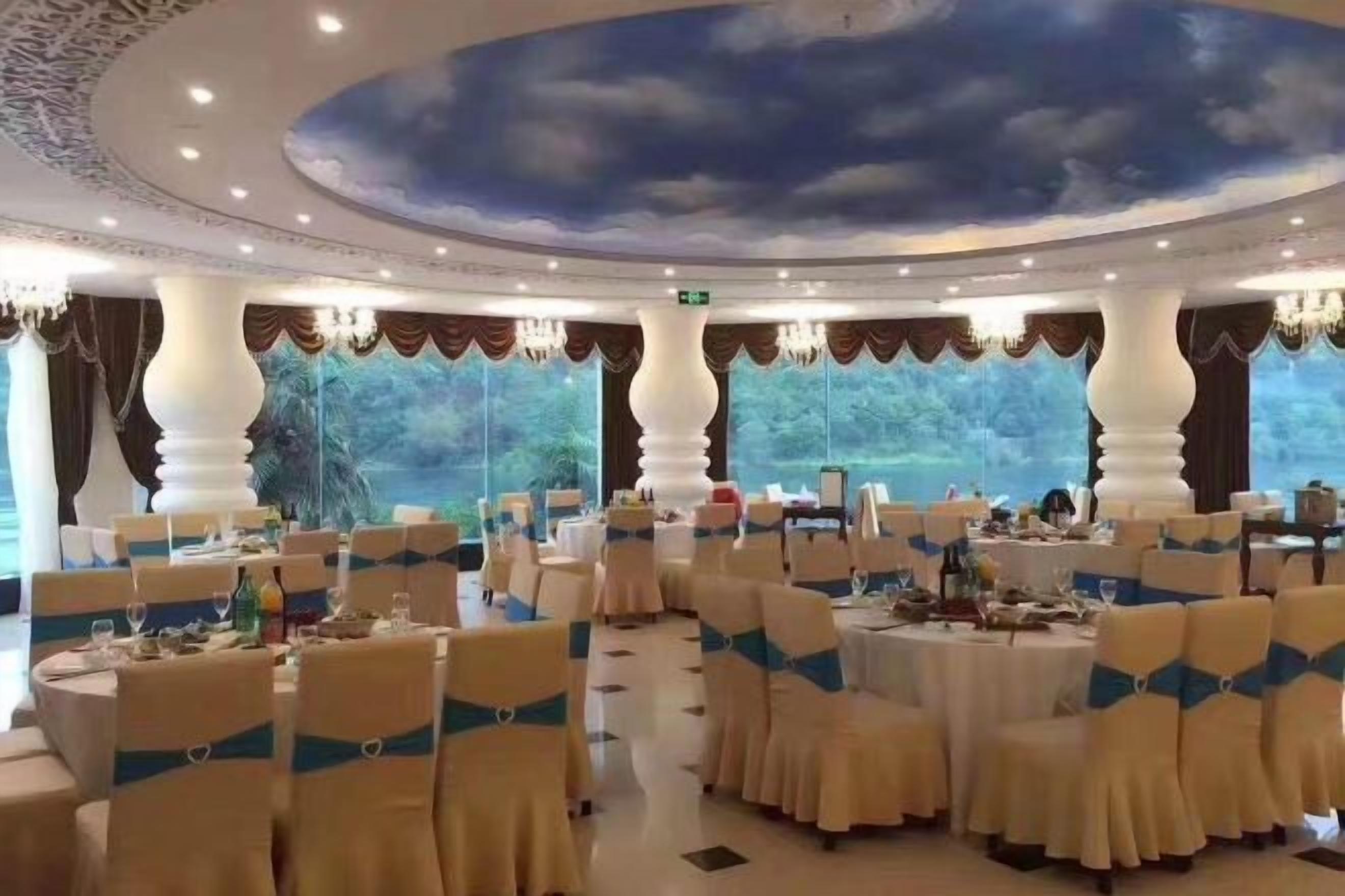 A banquet hall with round tables, chairs with blue sashes, and a ceiling mural.