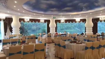 A banquet hall with round tables, chairs with blue sashes, and a ceiling mural.