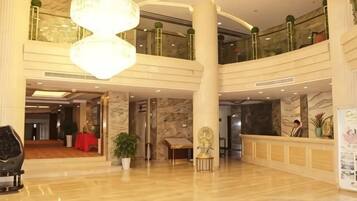 A spacious lobby with a high ceiling, marble flooring, and a reception desk.