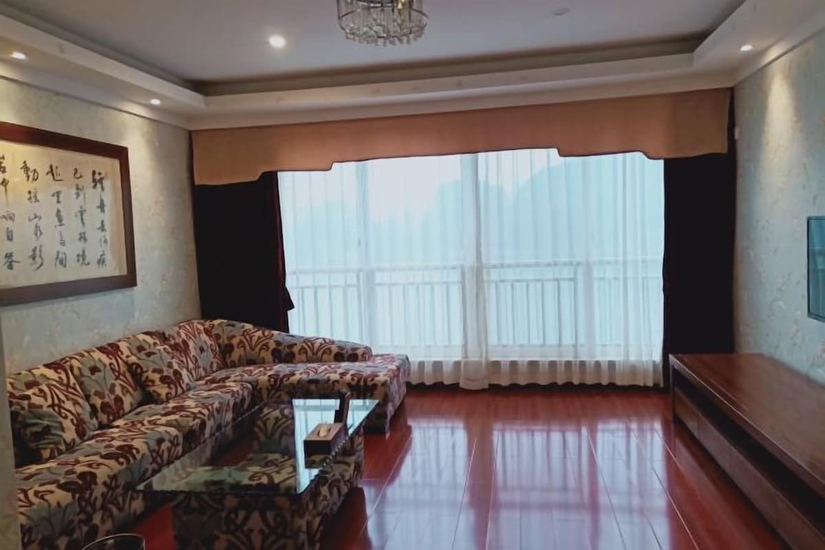 A living room with a sofa, a coffee table, and a large window with curtains.