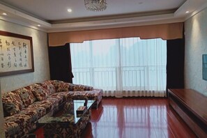 A living room with a sofa, a coffee table, and a large window with curtains. - Guorui Hotel (Jiande)