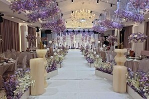 A formal event space with a central aisle, elegant lighting, and floral arrangements.