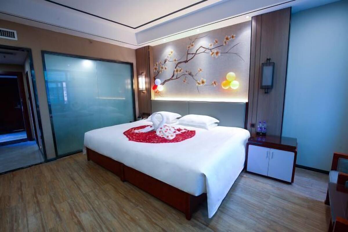Une chambre d’hôtel moderne dotée d’un grand lit, d’une table de chevet, d’une armoire et d’un mur décoratif orné d’un motif représentant une branche d’arbre.