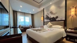 Ein Hotelzimmer mit einem großen Bett, einem Schreibtisch, einem Sessel, einem Fernseher und einem Gemälde an der Wand.
