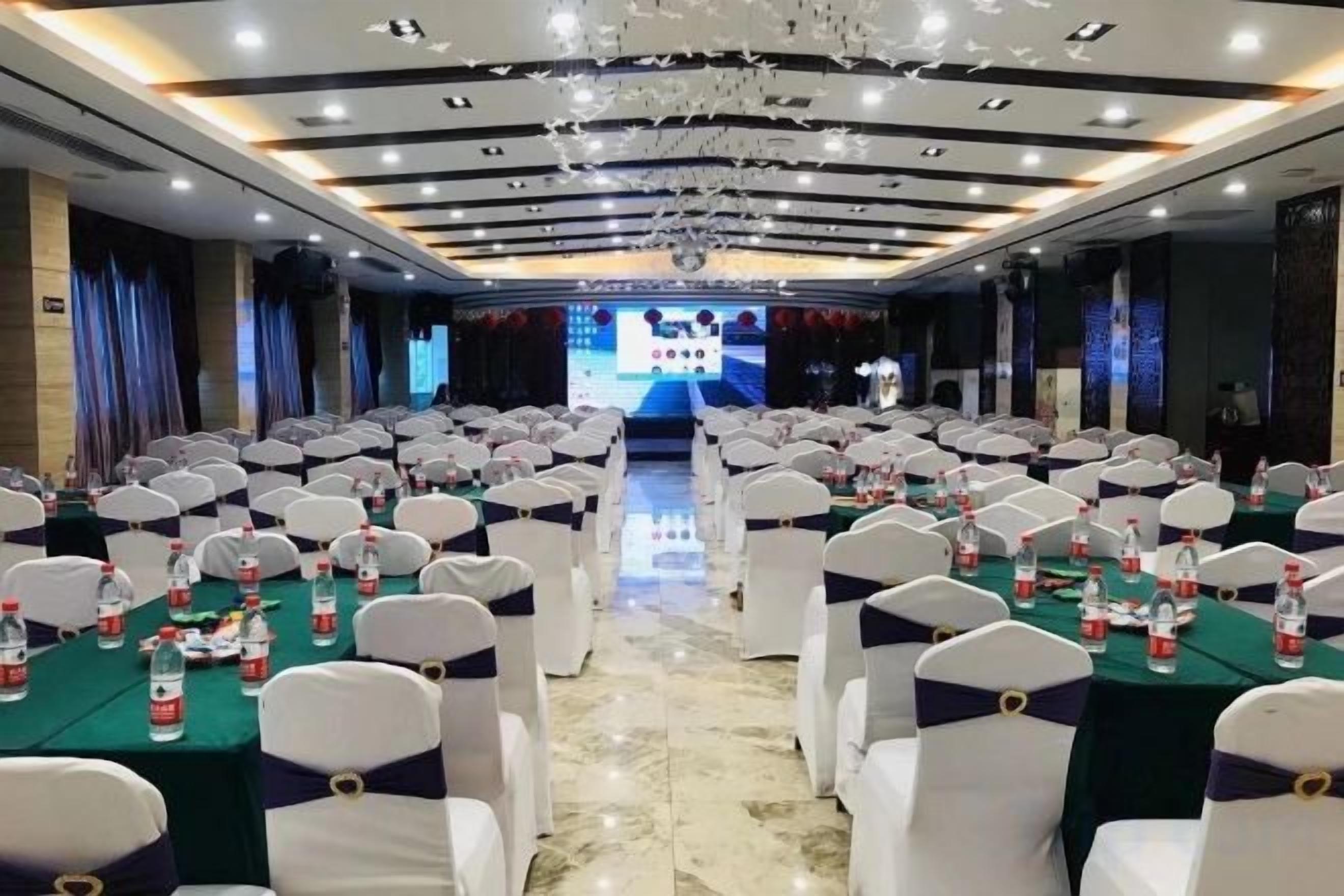 Un salón de conferencias con filas de mesas, sillas y un escenario al frente.