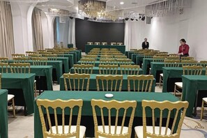 Une salle de conférence avec des rangées de tables et de chaises, une scène et un lustre.
